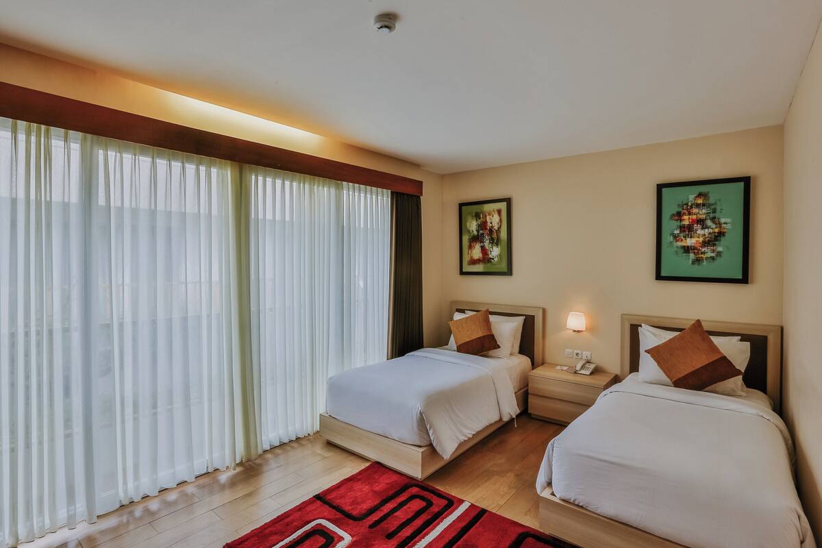 A hotel room with two beds, a nightstand with a lamp, and artwork on the walls.
