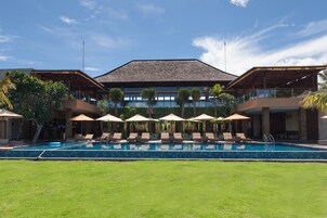 Um hotel com piscina, espreguiçadeiras, guarda-sóis e arquitetura de estilo tropical.