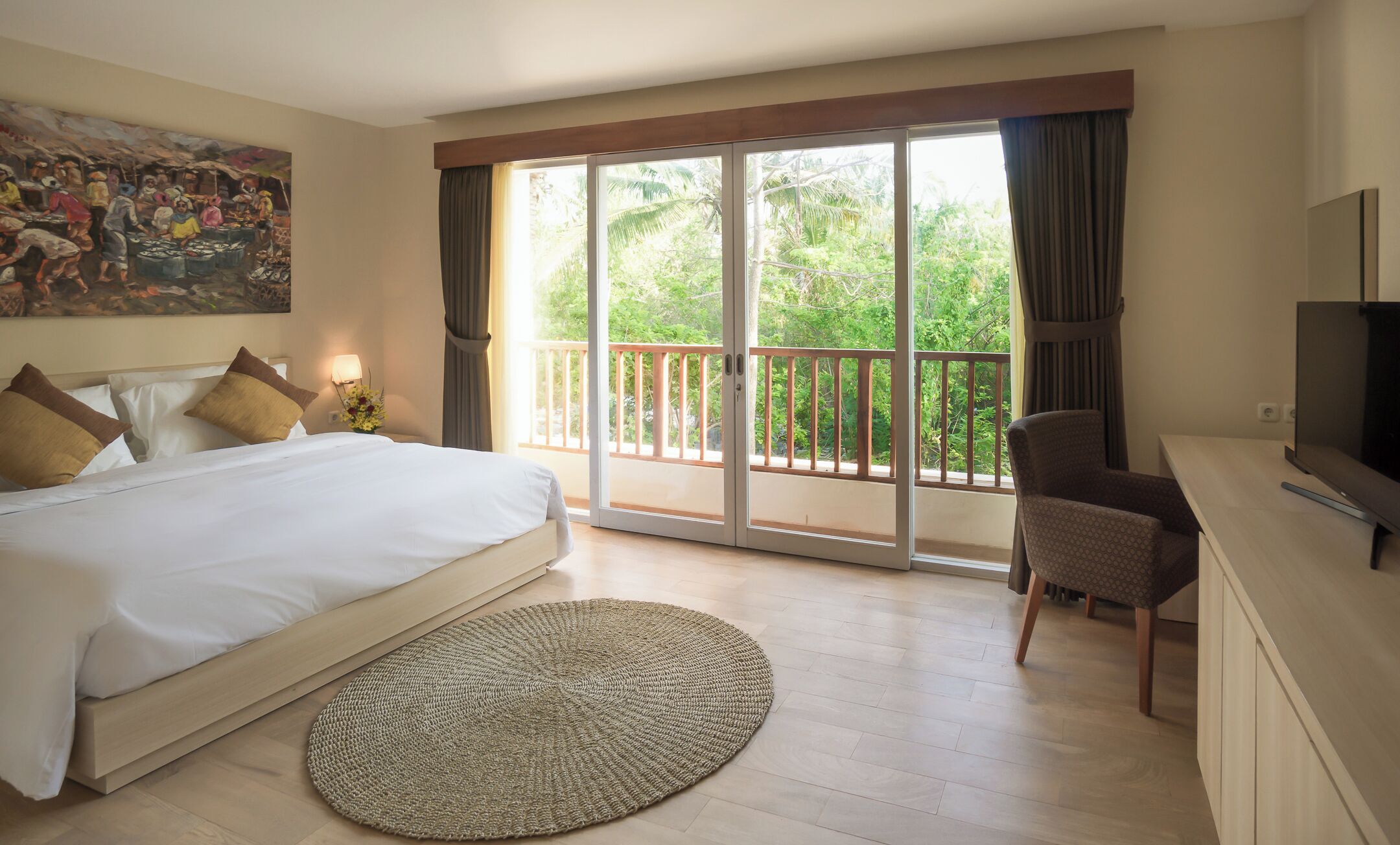 Habitación de hotel con una cama grande, televisión, una silla y balcón con vistas a zonas verdes.