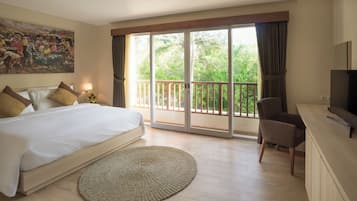 Habitación de hotel con una cama grande, televisión, una silla y balcón con vistas a zonas verdes.
