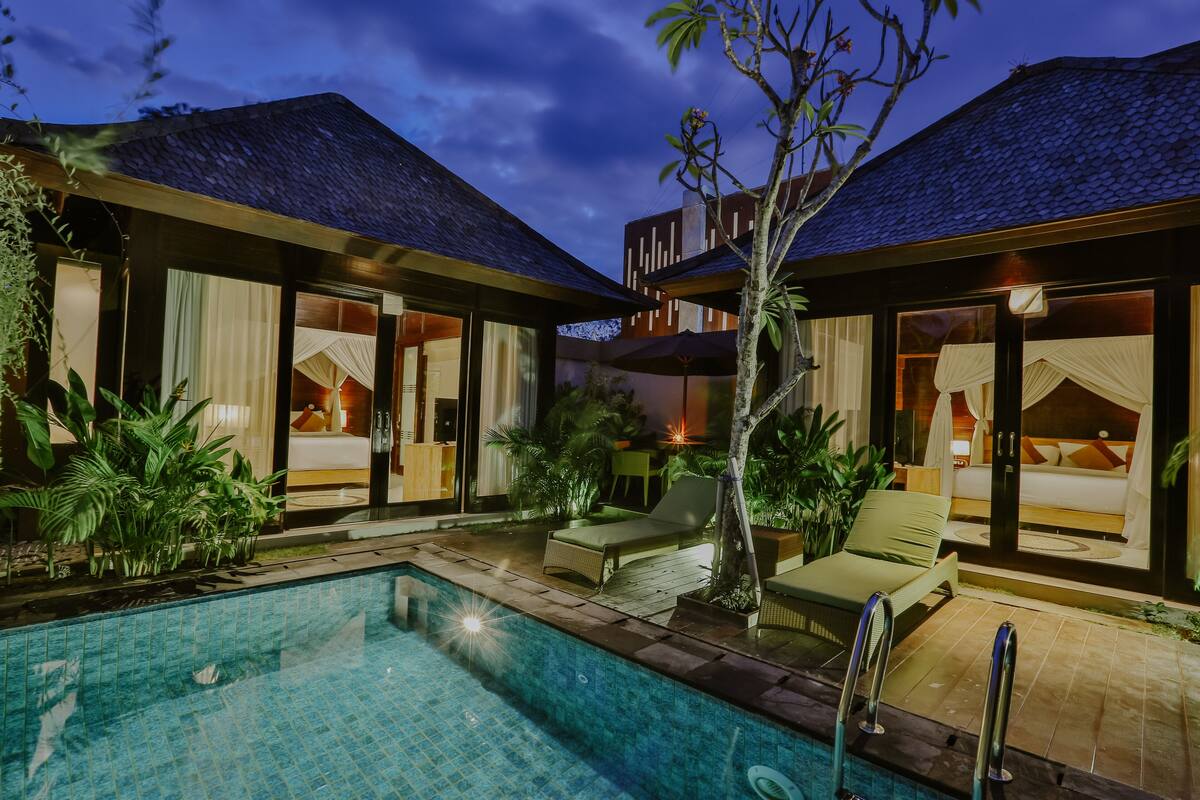 A modern hotel with a pool, outdoor seating, and a well-lit interior.