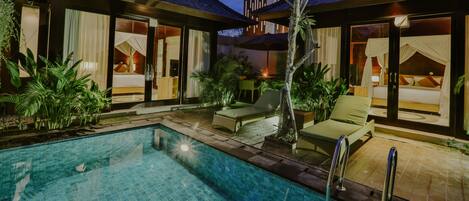 A modern hotel with a pool, outdoor seating, and a well-lit interior.