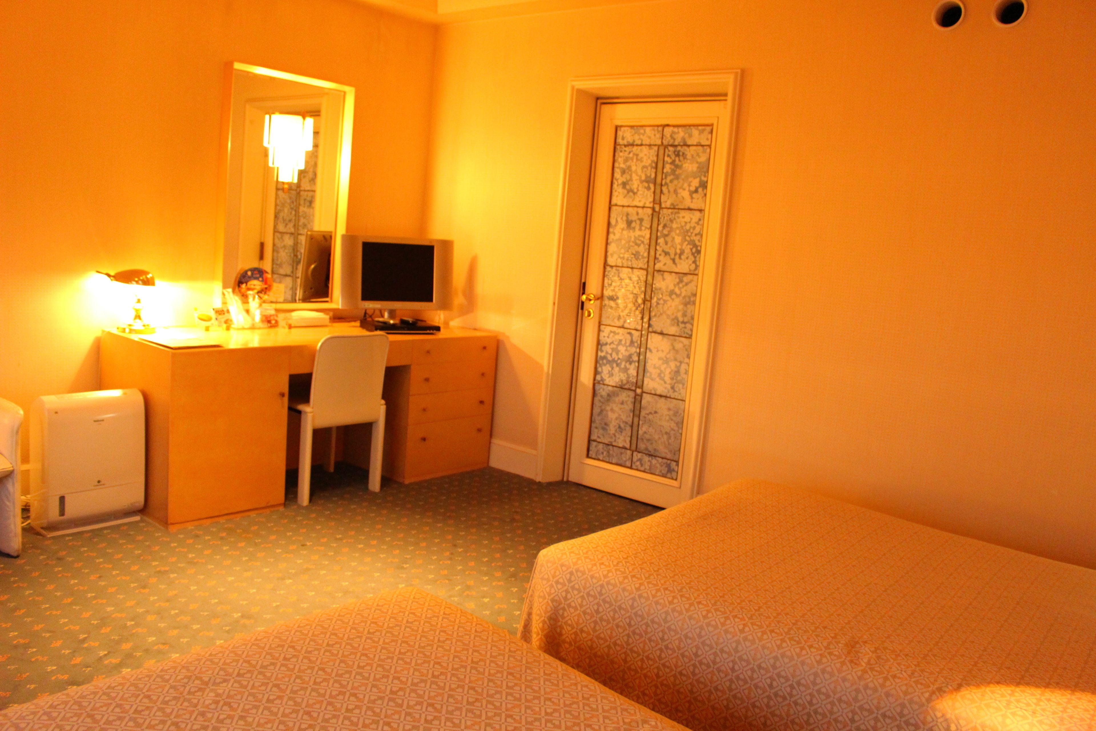 Habitación de hotel con cama, escritorio con computadora, una silla y una mesita de noche con lámpara.