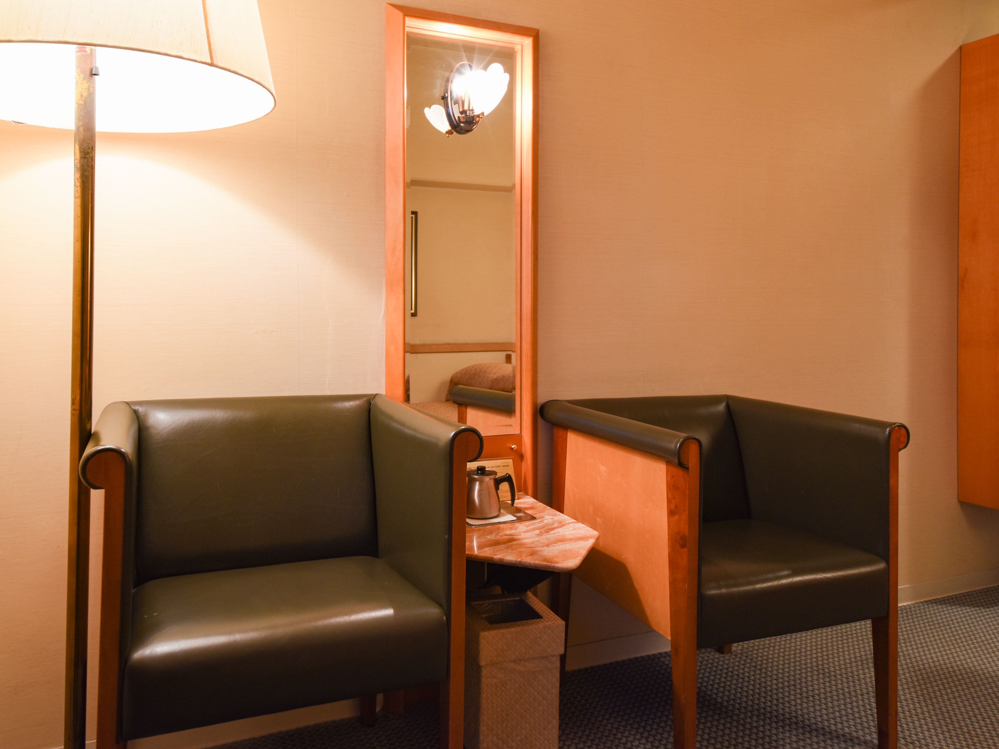 A small room with two leather armchairs, a wooden side table with a kettle, and a lamp.