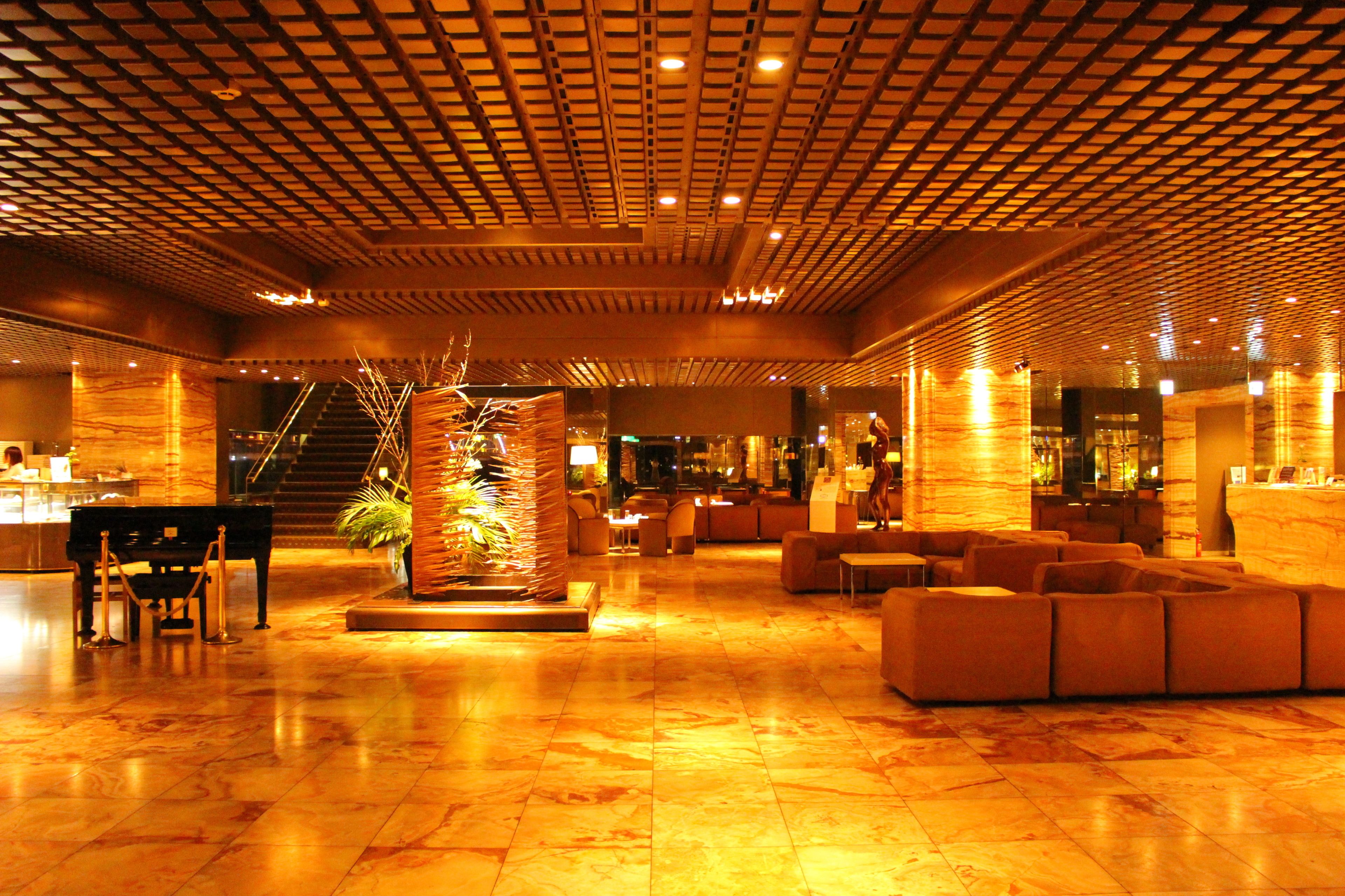 A spacious lobby with a grand piano, plush seating, and a decorative plant centerpiece.