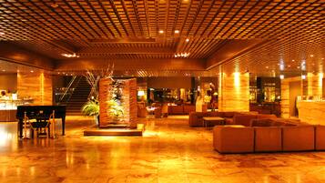 A spacious lobby with a grand piano, plush seating, and a decorative plant centerpiece.