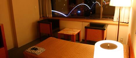 Ein Hotelzimmer mit Bett, Schreibtisch, Stuhl und Fenster mit Blick auf die Stadtlichter.