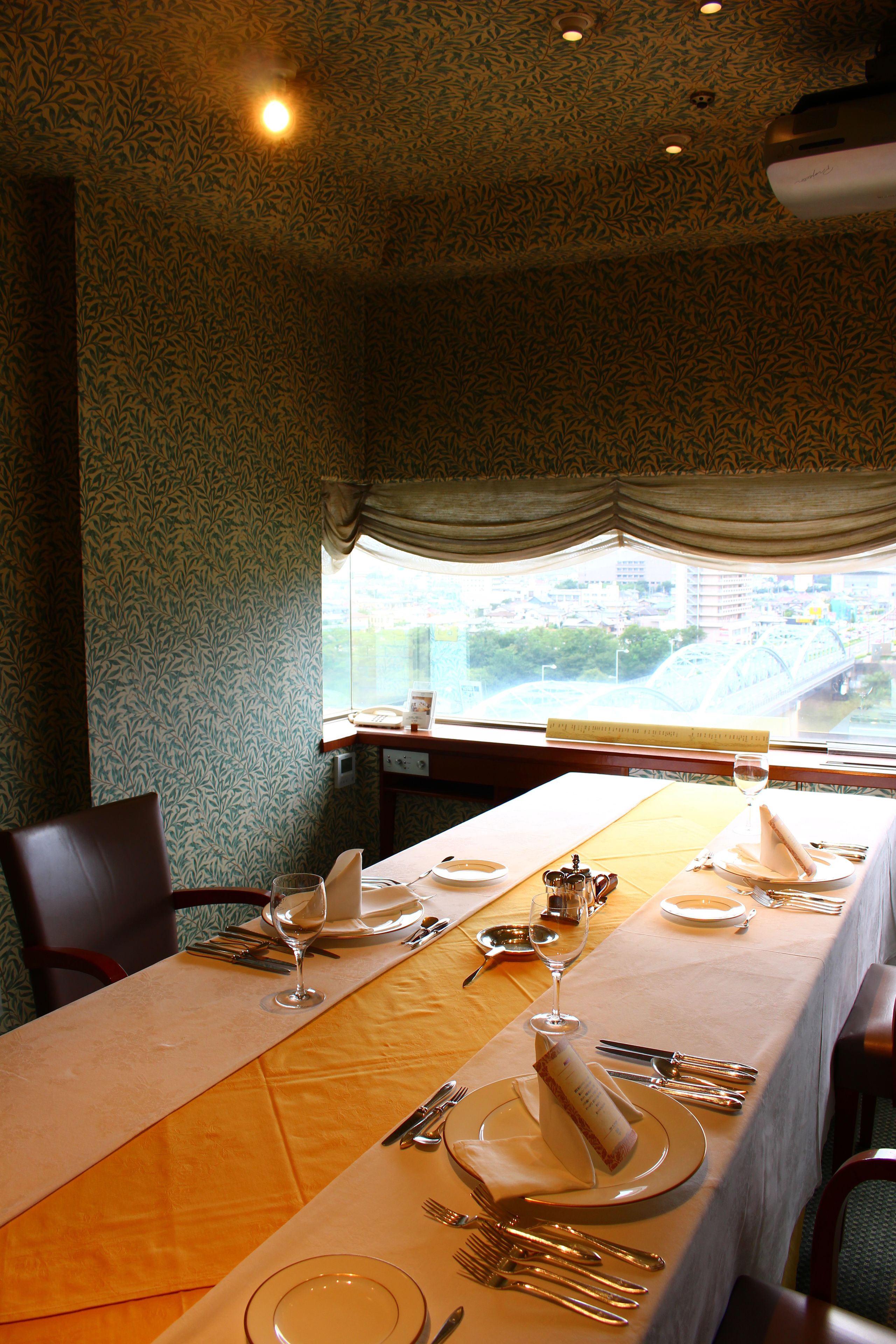 A dining table set for two with a view of a cityscape through a window.