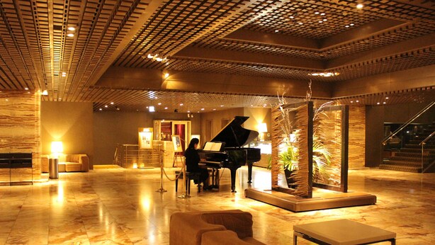 A spacious lobby with a grand piano, plush seating, and a decorative plant arrangement. - Gunma Royal Hotel (Maebashi)