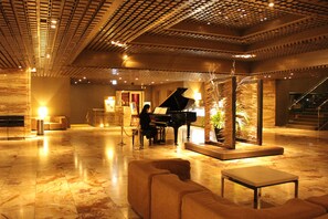 A spacious lobby with a grand piano, plush seating, and a decorative plant arrangement. - Gunma Royal Hotel (Maebashi)