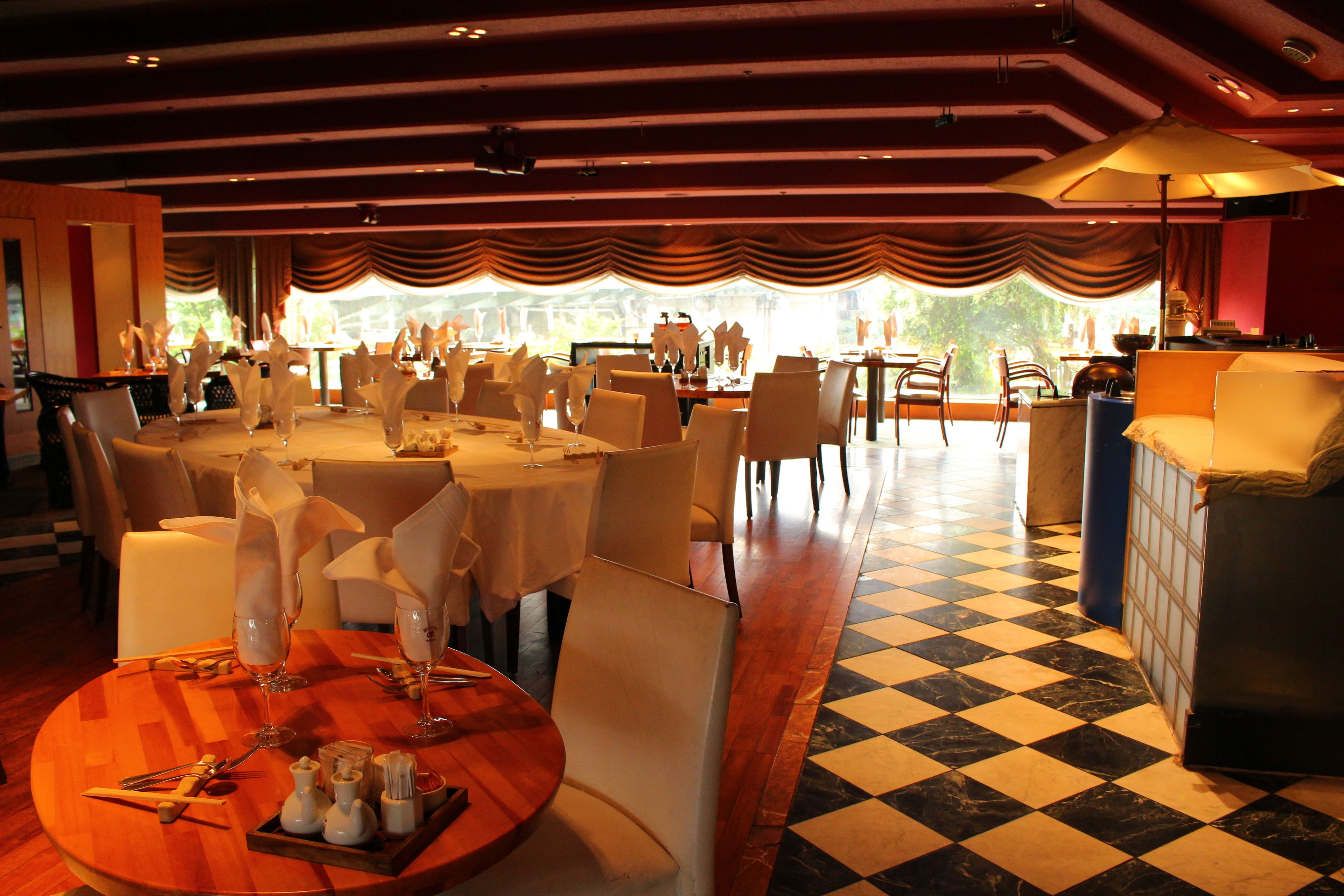 A dining area with round tables set for a meal, chairs, and a checkered floor.