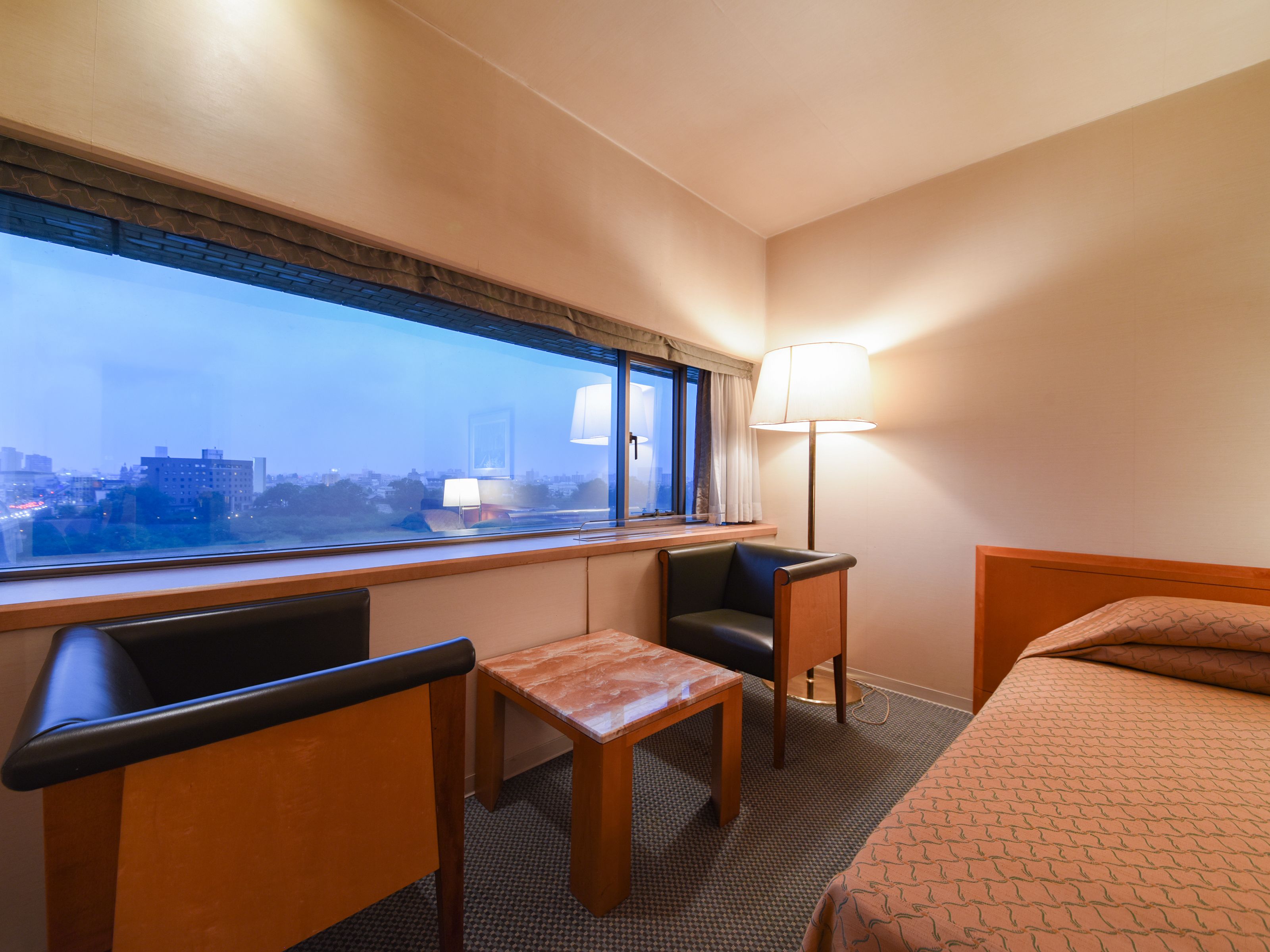 A hotel room with a bed, a desk, a chair, and a window with a city view.