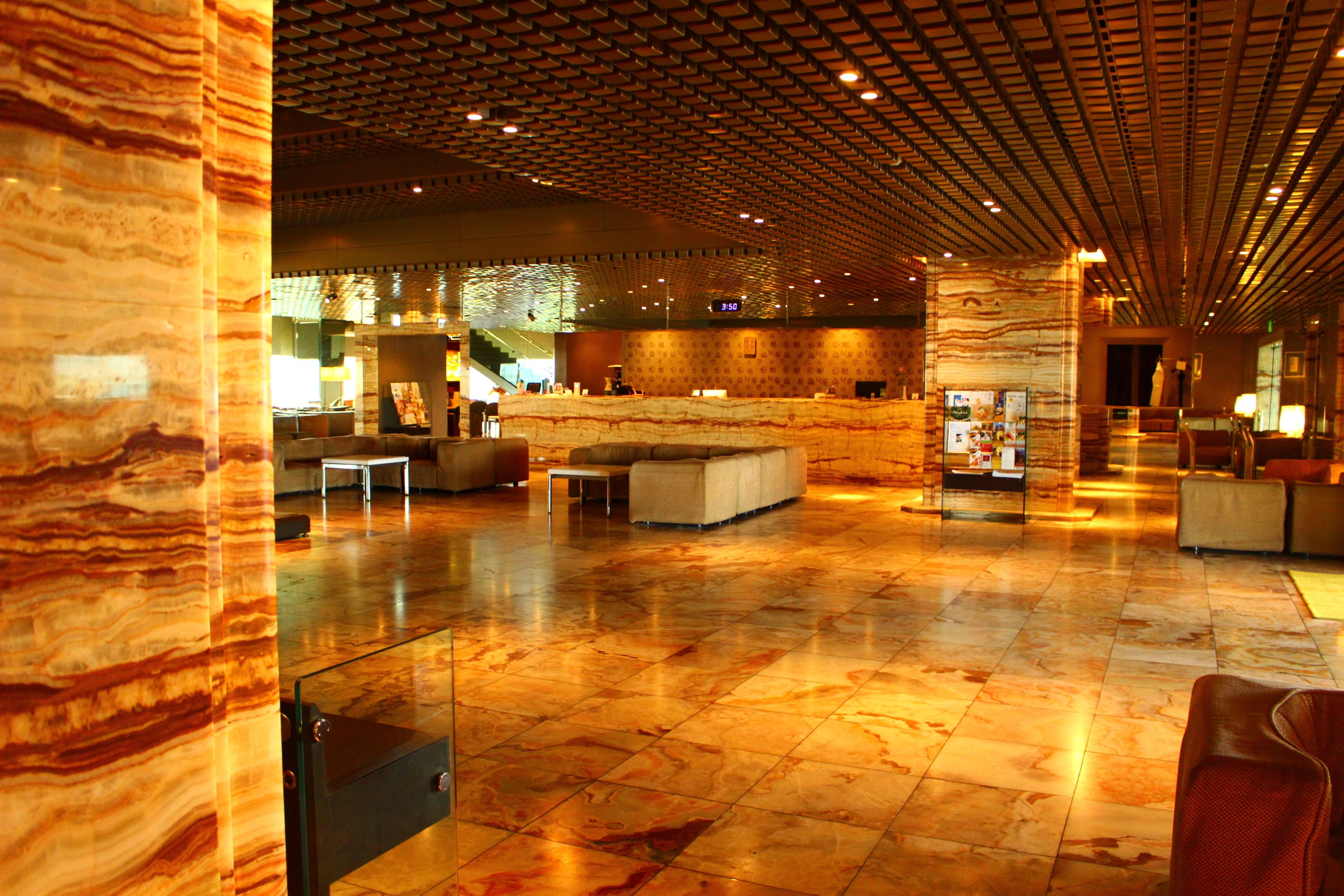 A spacious lobby with a marble floor, modern furniture, and a patterned ceiling.