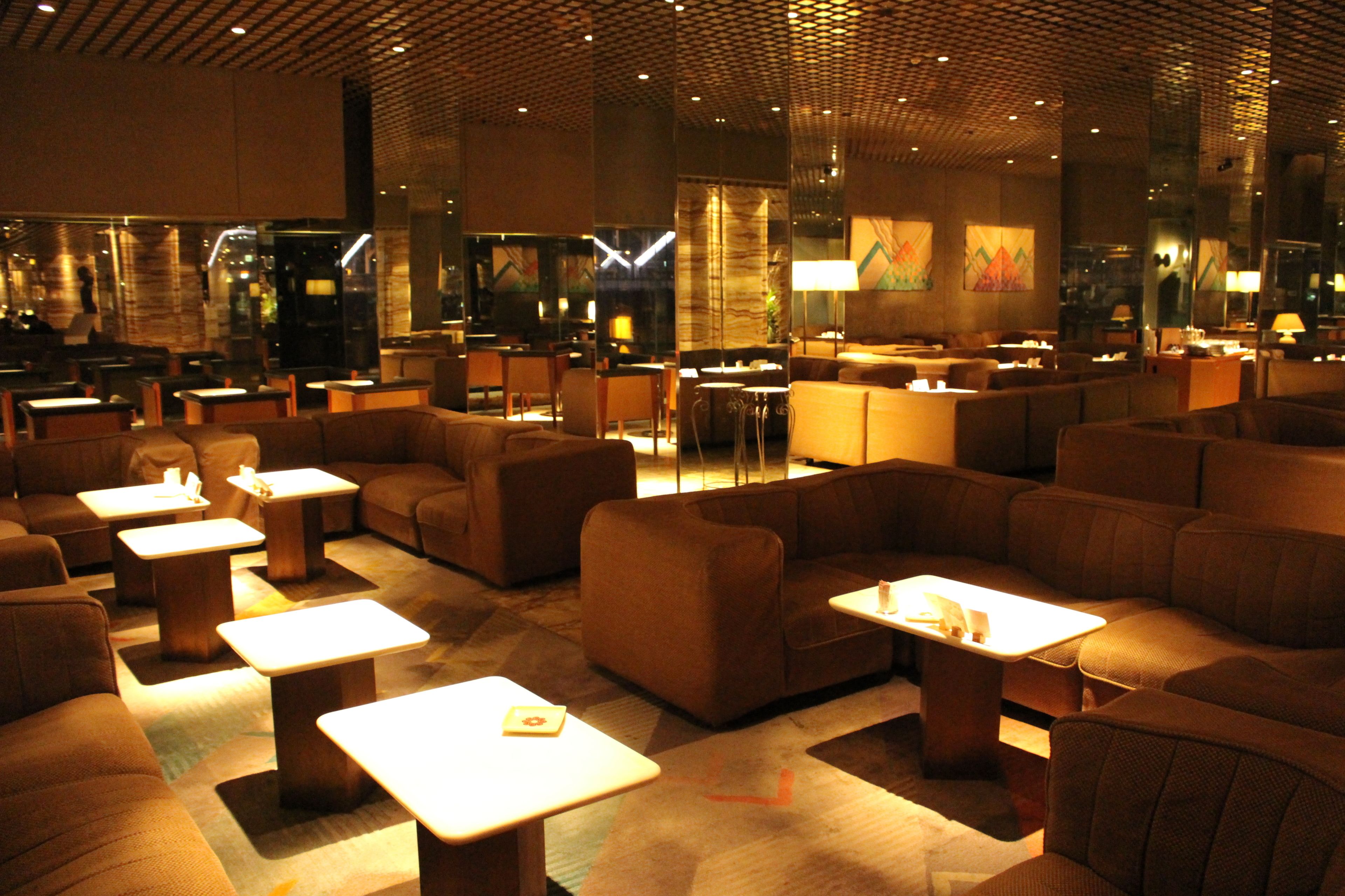Un hall d’hôtel moderne doté de plusieurs espaces de détente, notamment des canapés et des tables, et un bar situé au fond de la pièce.