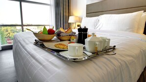 A hotel room with a large bed, a tray with breakfast items, a window with a view of greenery, and a lamp on the nightstand. - Space Apartments (Dhaka)