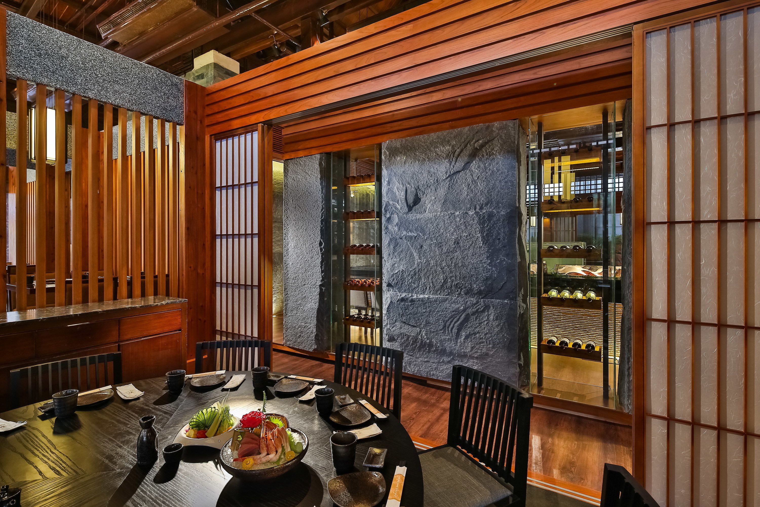 A traditional Japanese dining room with a wooden table, black chairs, and a stone wall.