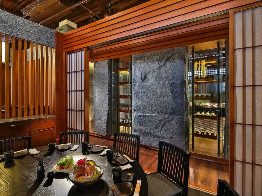 A traditional Japanese dining room with a wooden table, black chairs, and a stone wall.