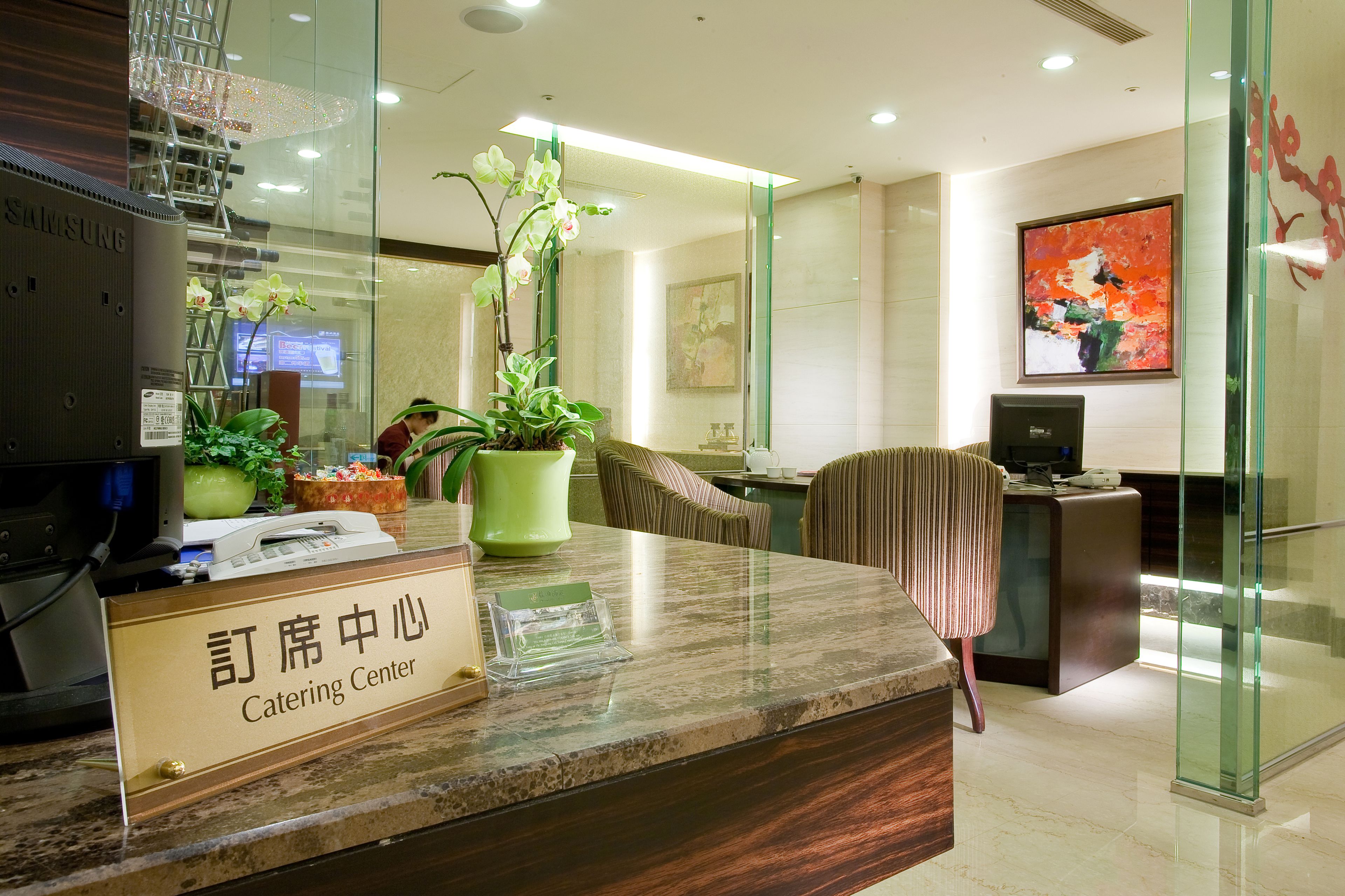 A modern reception area with a marble counter, a potted orchid, and a sign reading "Catering Center".