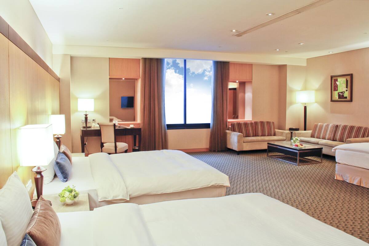 Ein Hotelzimmer mit zwei Betten, einer Couch, einem Schreibtisch und einem großen Fenster.