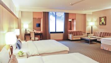 A hotel room with two beds, a sofa, a desk, and a large window.