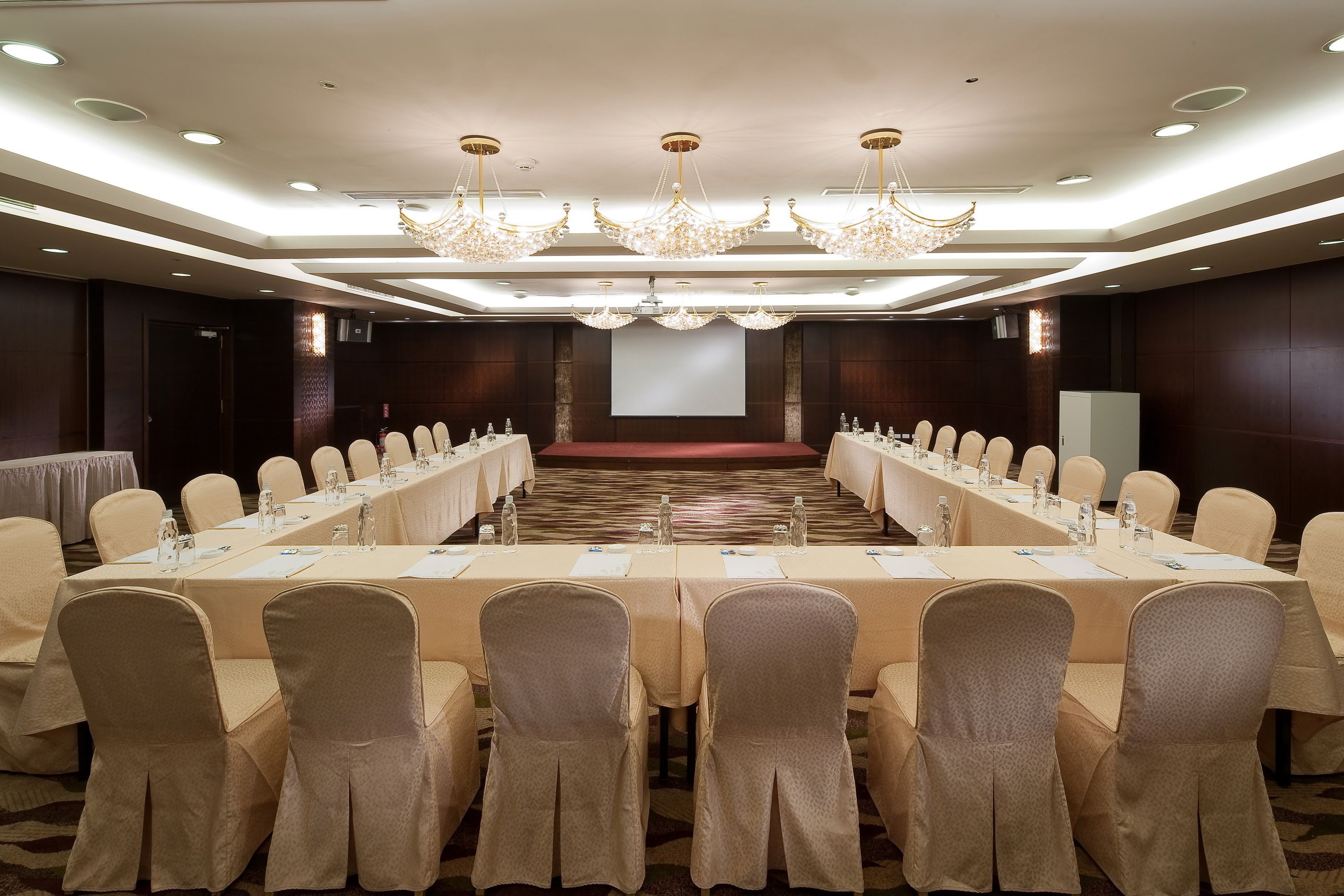 Un salón de conferencias con una larga mesa, sillas y una pantalla para proyector.