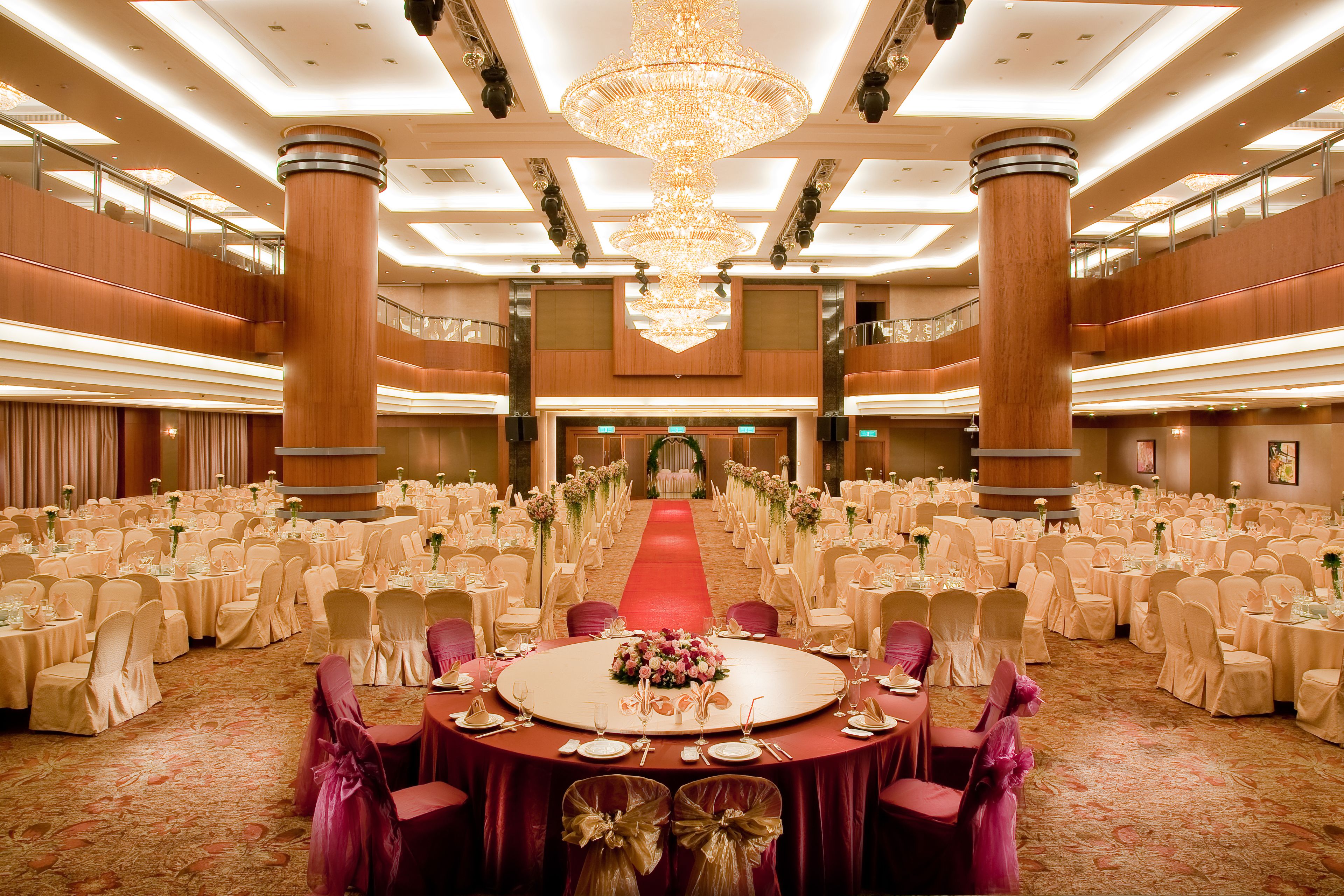 A large ballroom with a central round table, multiple rows of round tables, and a red carpet leading to a stage.