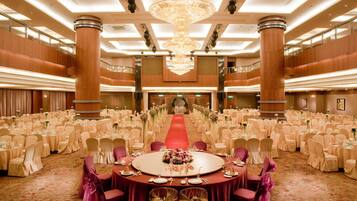 A large ballroom with a central round table, multiple rows of round tables, and a red carpet leading to a stage.