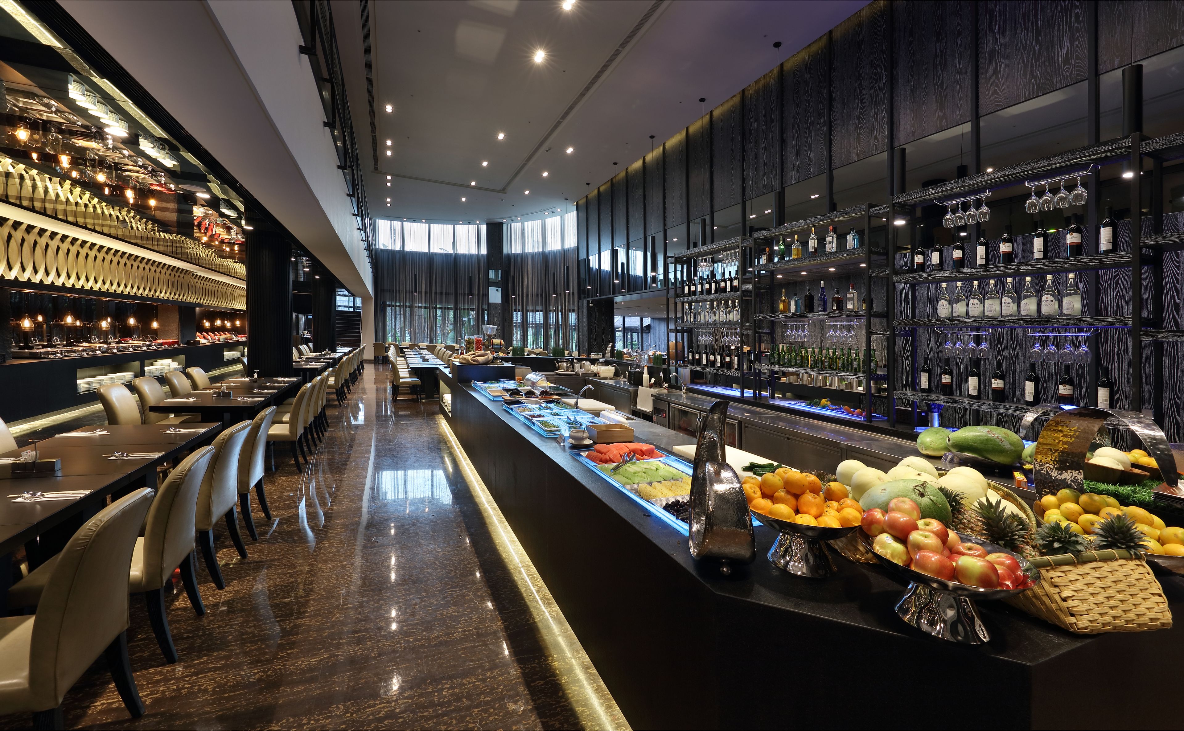 A modern bar area with a long counter, various food items, and a selection of bottles and glasses.