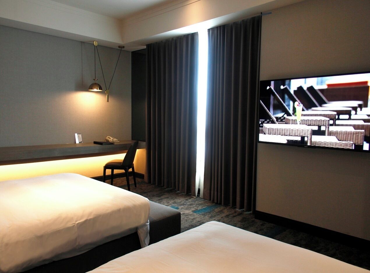 Habitación de hotel con dos camas, un escritorio, una silla, un televisor y una ventana con cortinas.