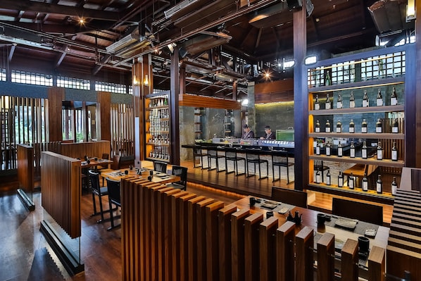 A modern bar area with wooden partitions, a bar counter, and shelves displaying bottles.