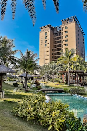 A hotel with a large pool, palm trees, and a clear blue sky.