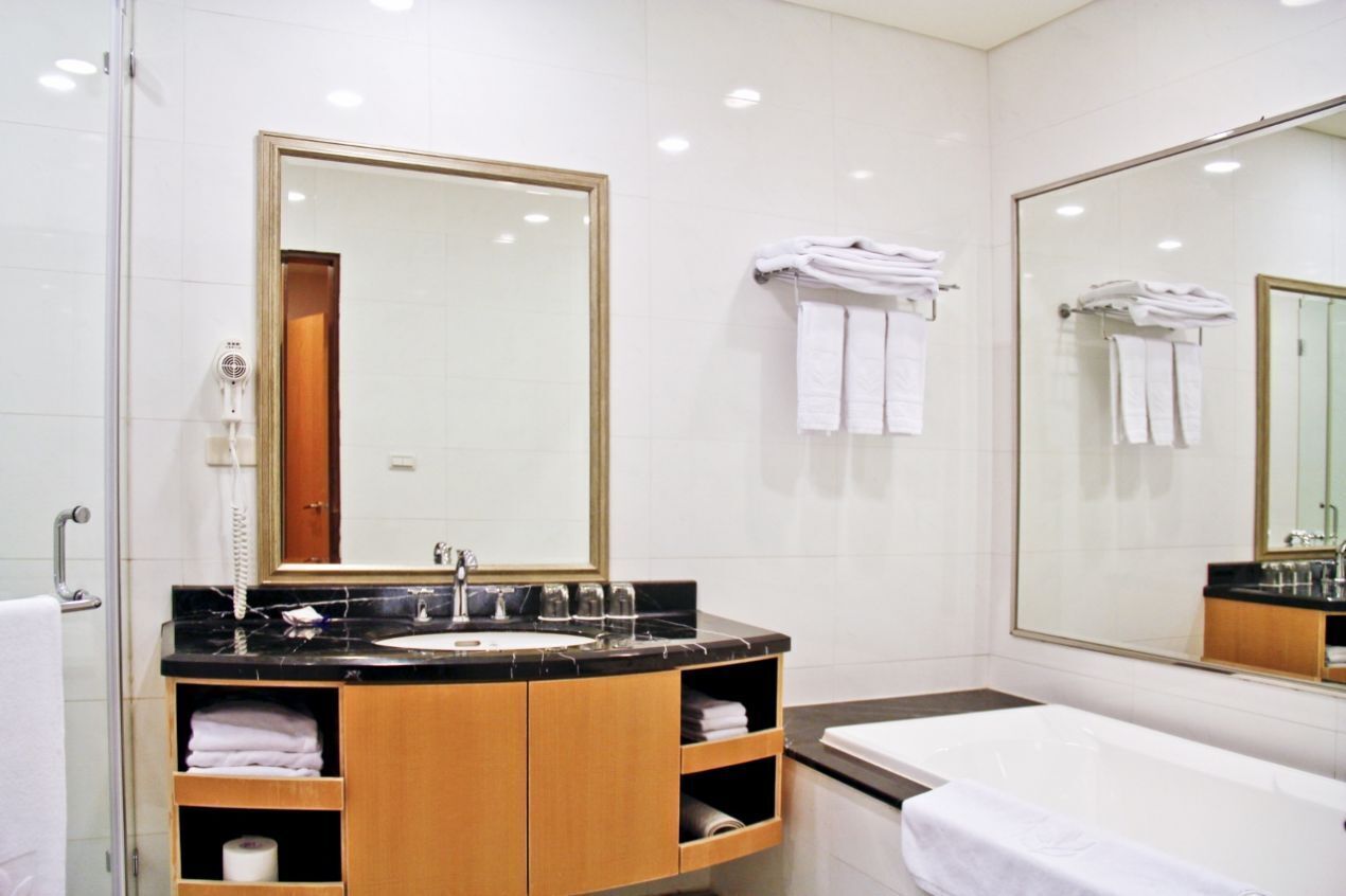 Een moderne badkamer met een grote spiegel, een wastafel en een badkuip. Handdoeken en een toiletpapierrol zijn zichtbaar.
