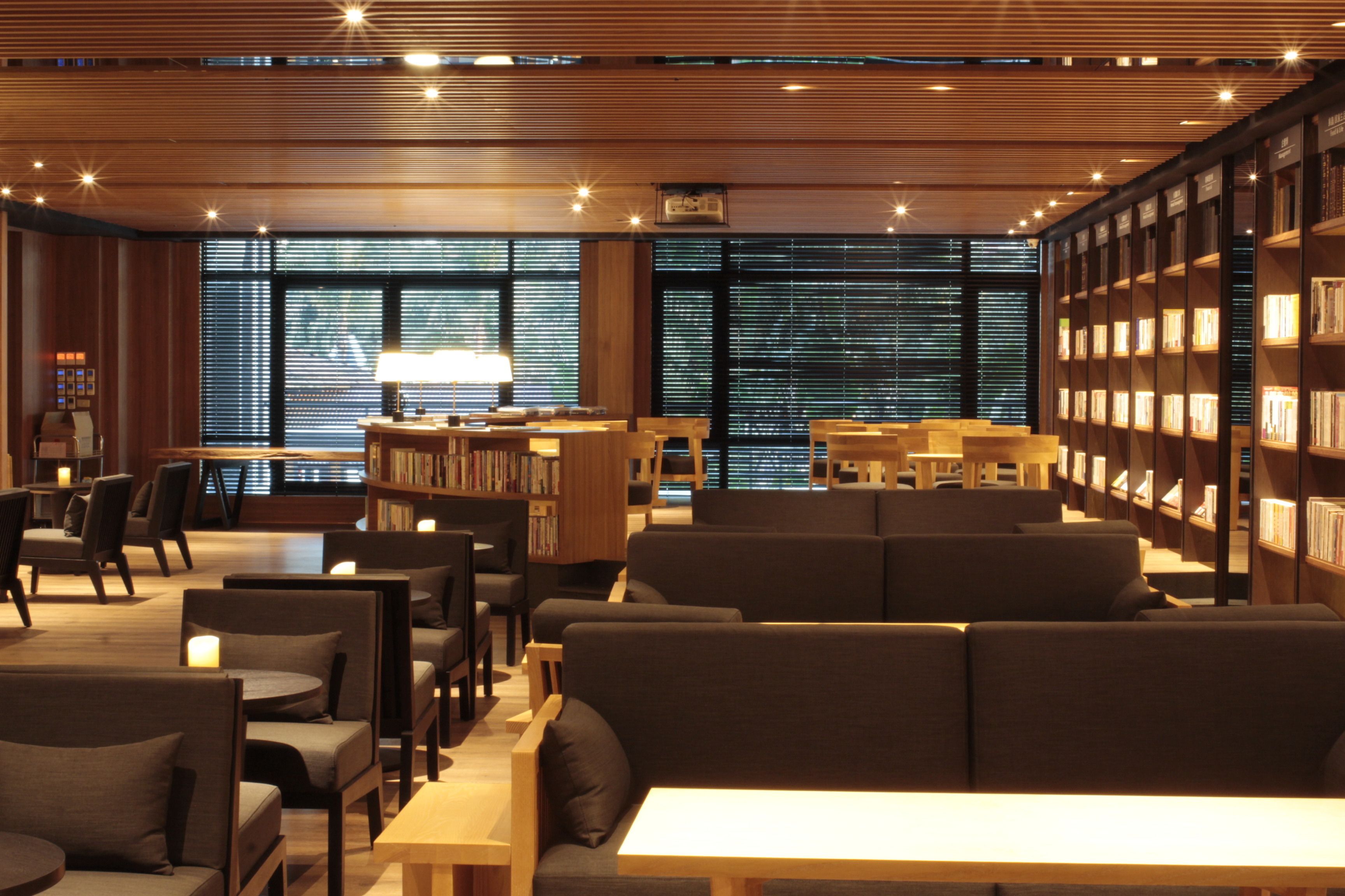 A modern library with wooden bookshelves, comfortable seating, and large windows.