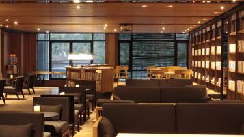 A modern library with wooden bookshelves, comfortable seating, and large windows.