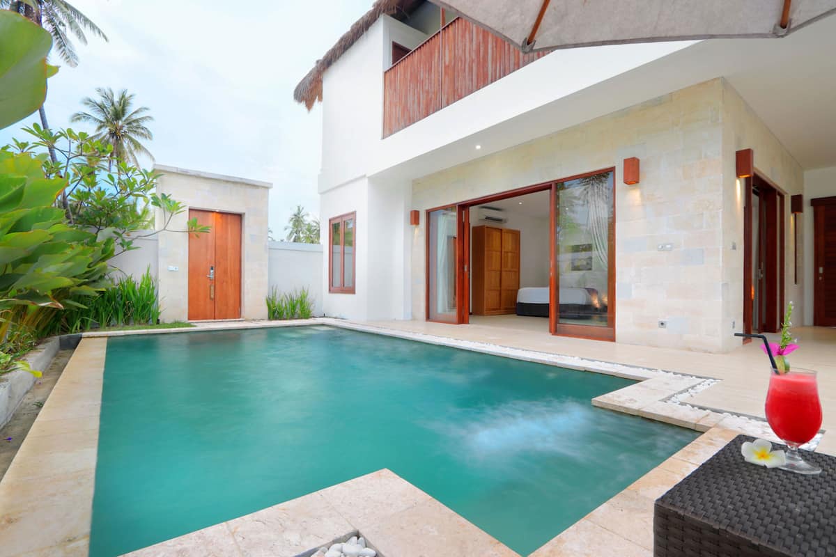 A modern pool area with a clear pool, a wooden door, and a glass door leading to a covered patio.