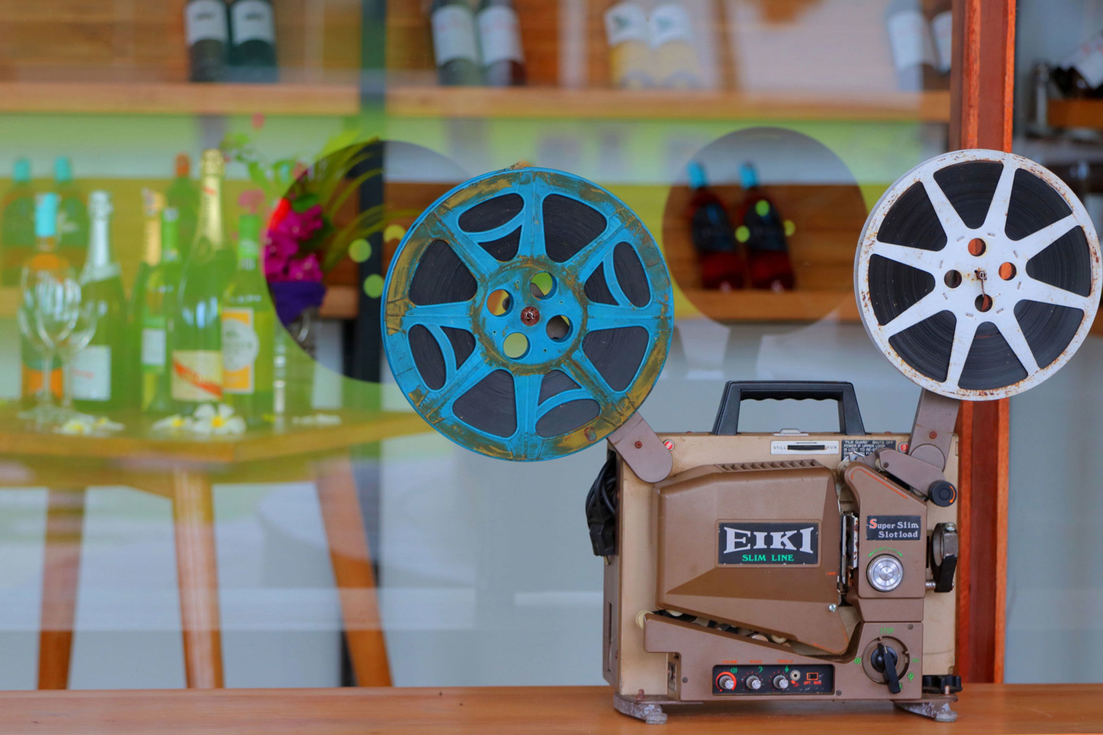 A vintage film projector with a beige body and blue reel, placed on a wooden table.