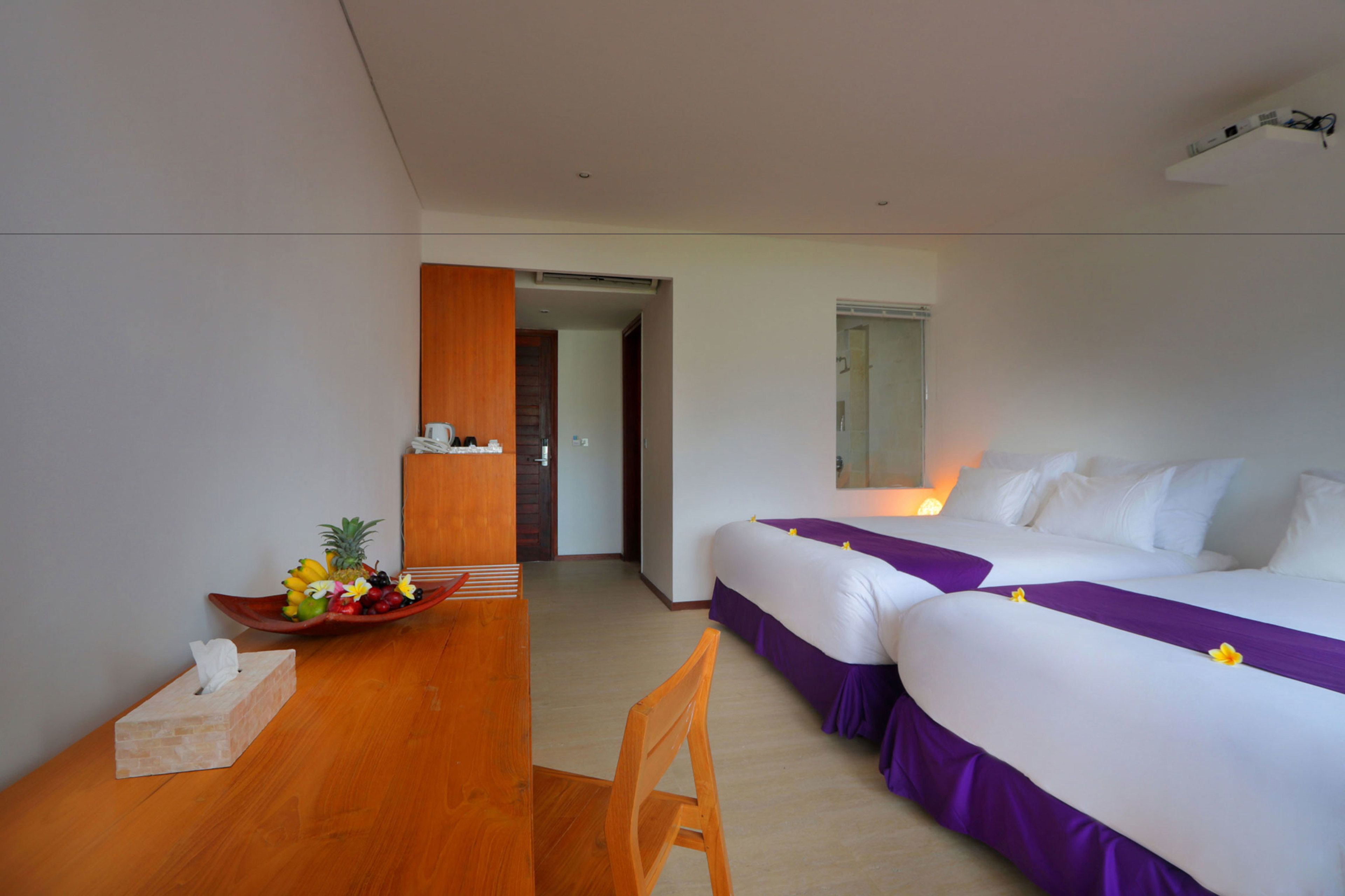 A hotel room with two beds, a wooden desk, a small table with a tissue box, and a bowl of fruit.