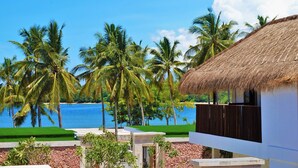 A beachfront property with a thatched-roof building, palm trees, and a clear view of the sea. - Anema Wellness & Resort (Tanjung)