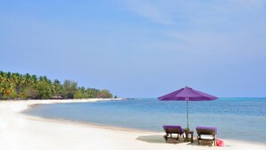 A beach with two lounge chairs and a purple umbrella, a clear sky, and a calm sea. - Anema Wellness & Resort (Tanjung)