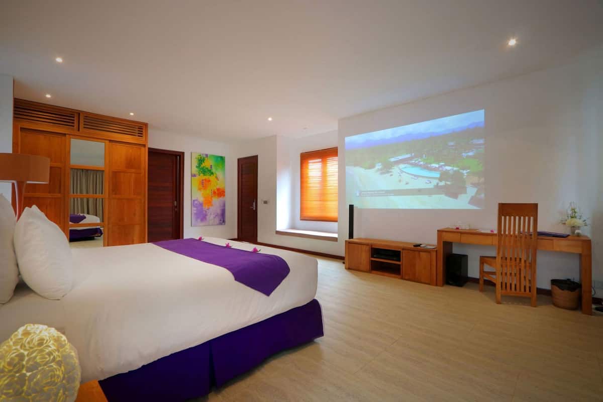 A bedroom with a bed, a desk, a chair, a projector screen, and a window with blinds.