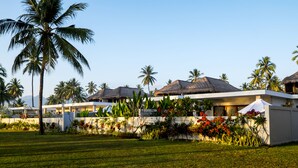 A resort with thatched-roof buildings, palm trees, and a well-maintained lawn. - Anema Wellness & Resort (Tanjung)