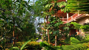 A lush garden pathway leading to a building with a red railing balcony. - Hotel Royal Safari (Sauraha)