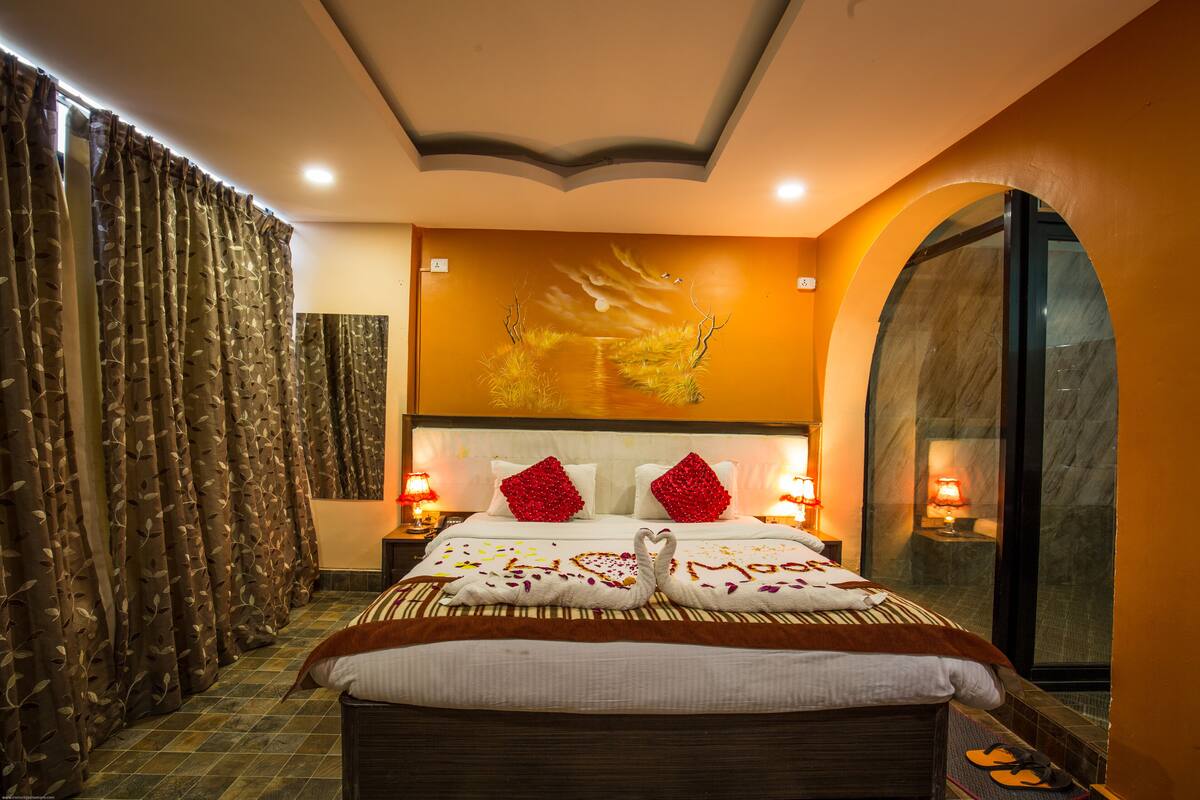 A hotel room with a large bed, two bedside lamps, a mural on the wall, and a large window.