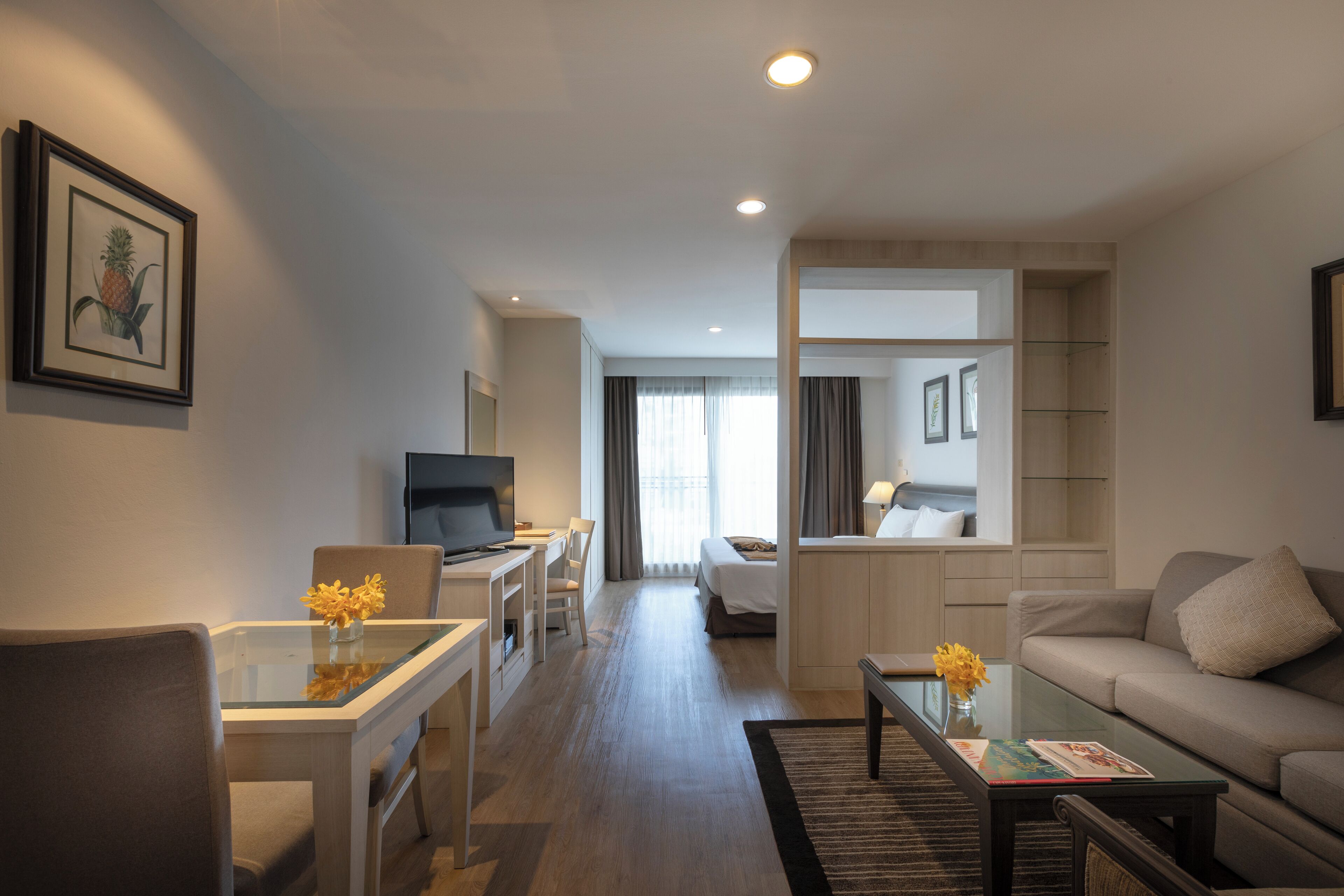 Habitación de hotel moderna con una mesa de vidrio para comer, un sofá, un televisor y una cama con vistas al exterior.