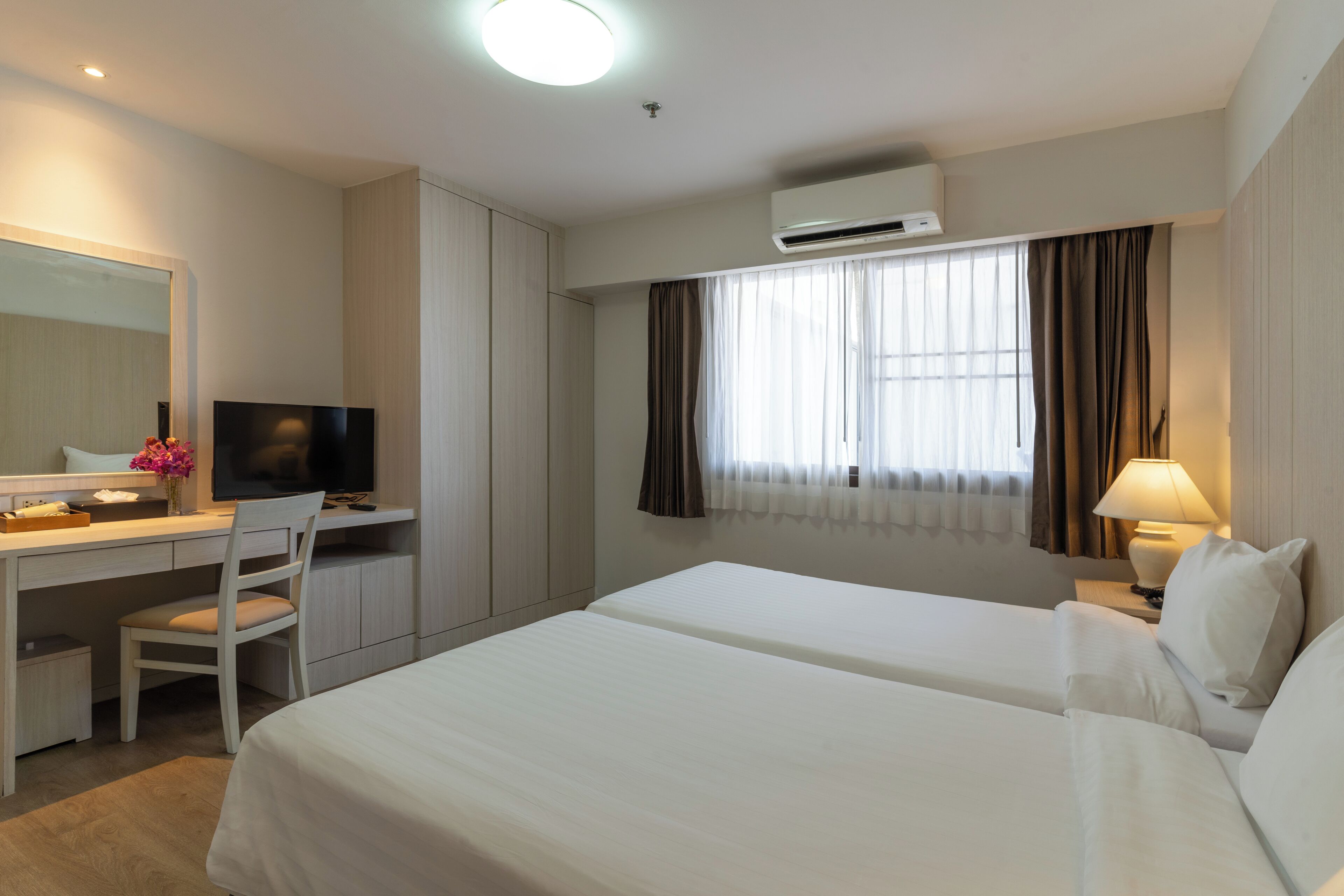 A hotel room with a bed, a desk with a chair, a television, and an air conditioning unit.