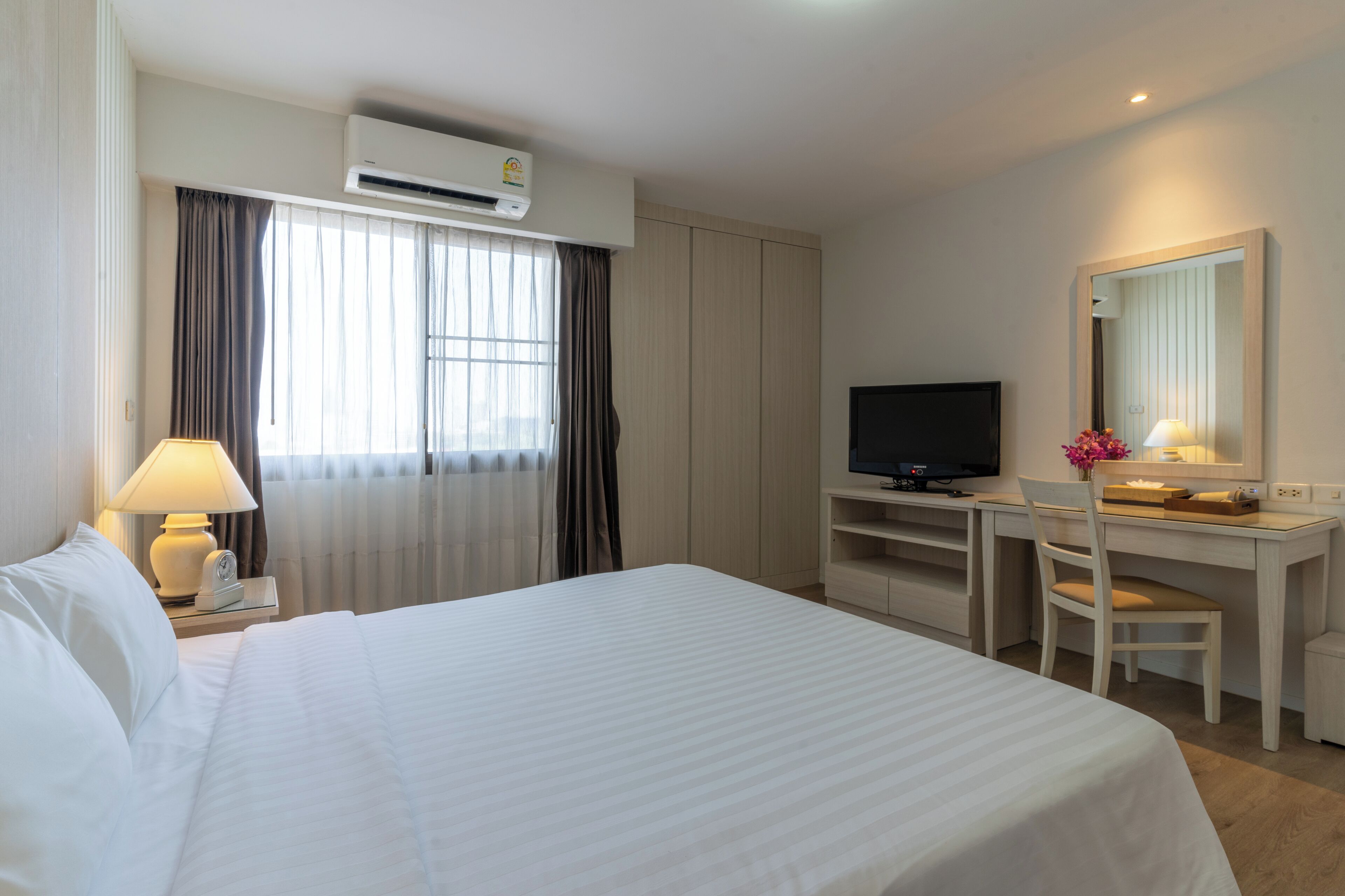 A hotel room with a bed, a desk, a television, and an air conditioning unit.