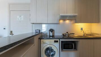 A compact kitchen with a washing machine, microwave, and a coffee maker.