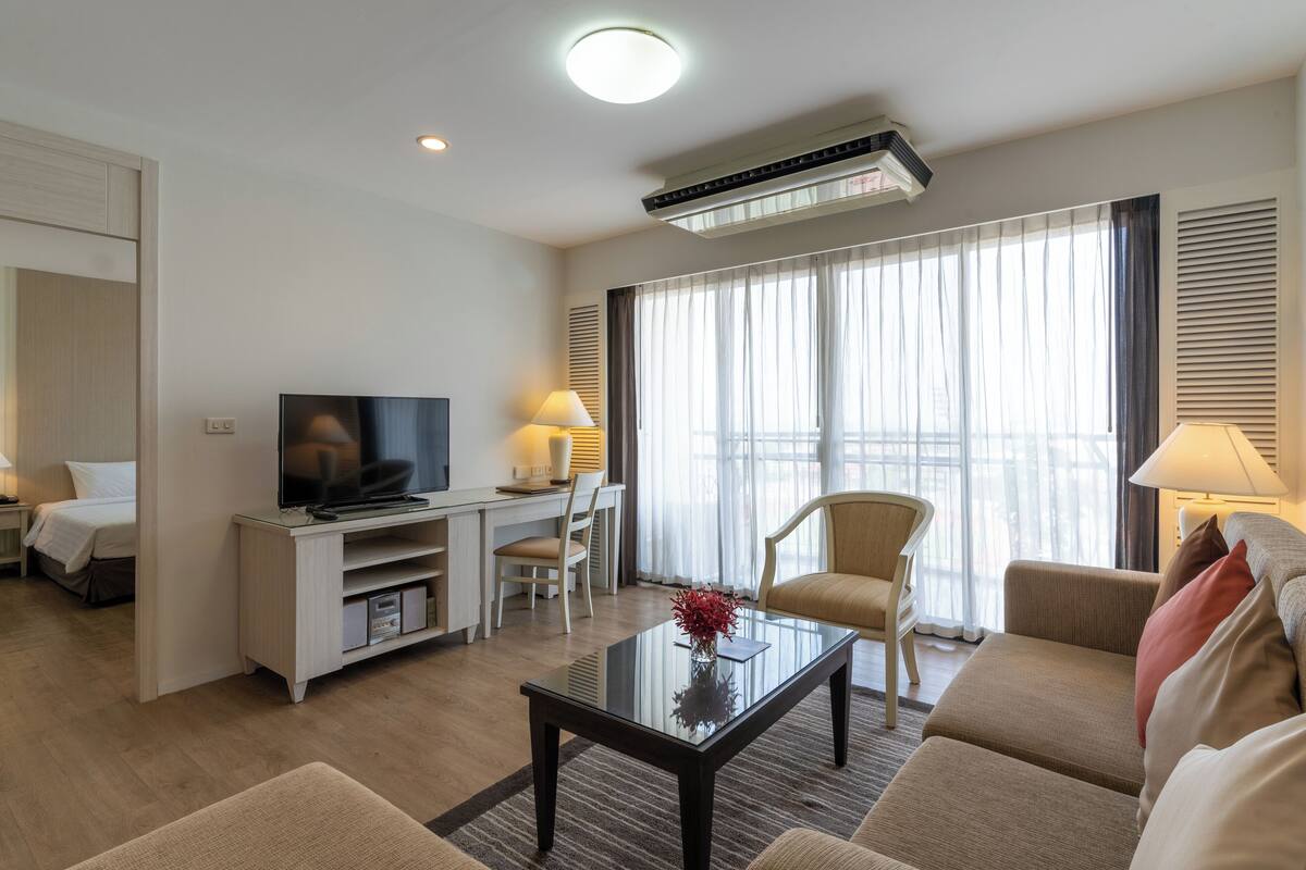 Ein modernes Hotelzimmer mit Flachbildfernseher, einer Couch, einem Couchtisch und einem Schreibtisch mit Lampe.