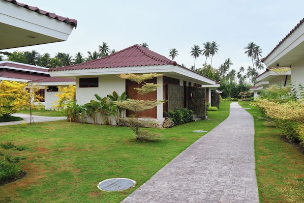 A pathway leading to a building with a red roof, surrounded by lush greenery and palm trees. - Dolores Tropicana Resort (General Santos)