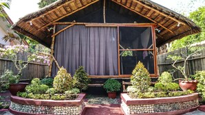 Una casa de madera tradicional con techo de paja, ventanas amplias y un jardín con diversas plantas y un sendero de piedra.